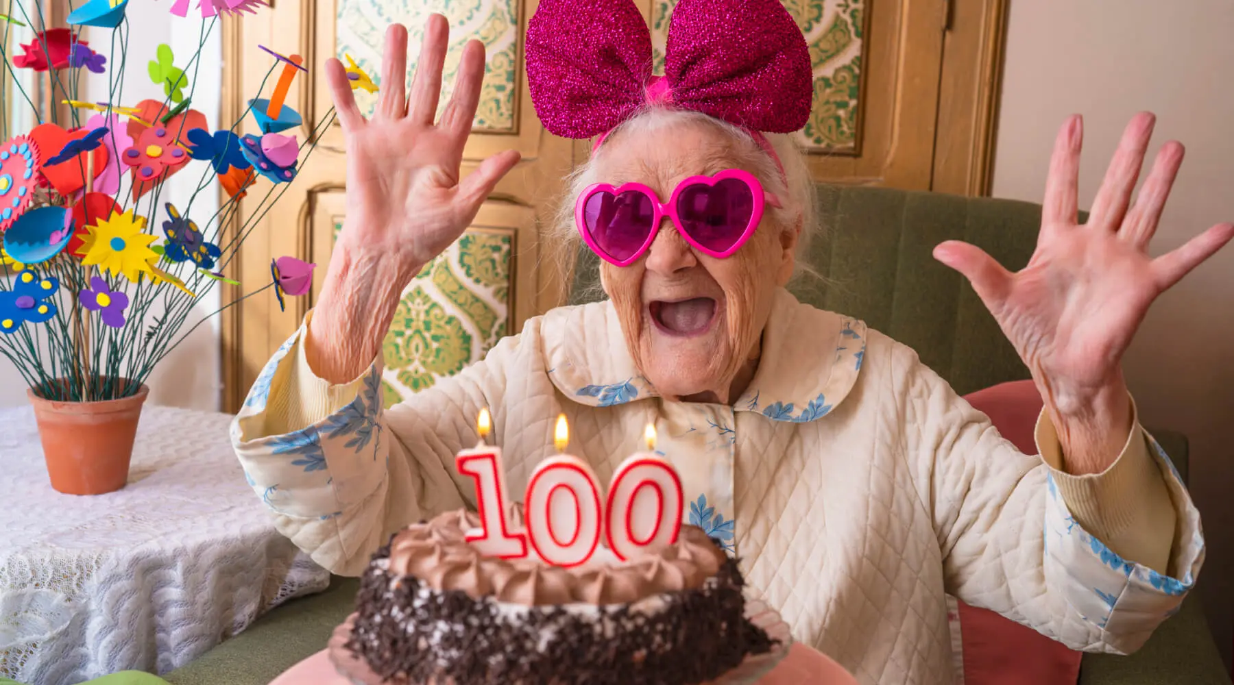 Elderly woman wearing heart shaped sunglasses and a ribbon headband celebrating her 100th birthday