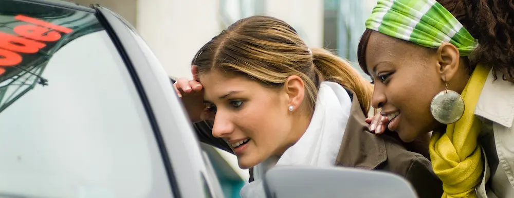 Two young women looking into the window of a car they're considering buying