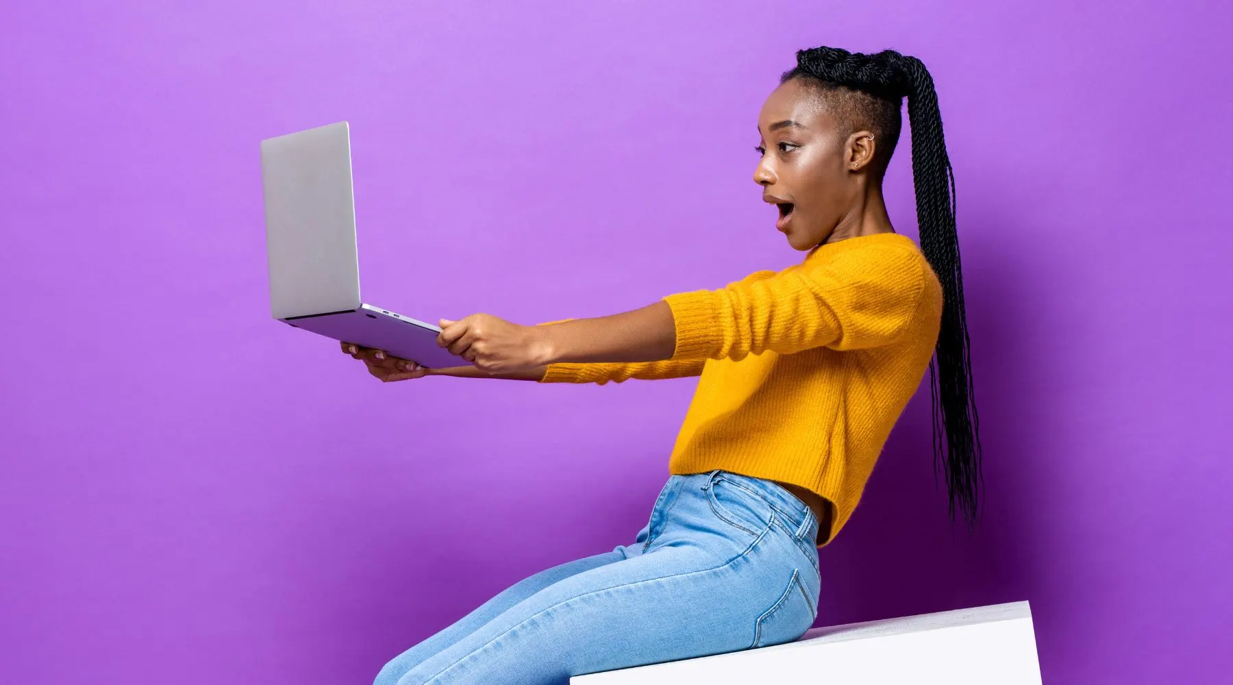 Surprised woman looking at laptop against a purple backdrop.