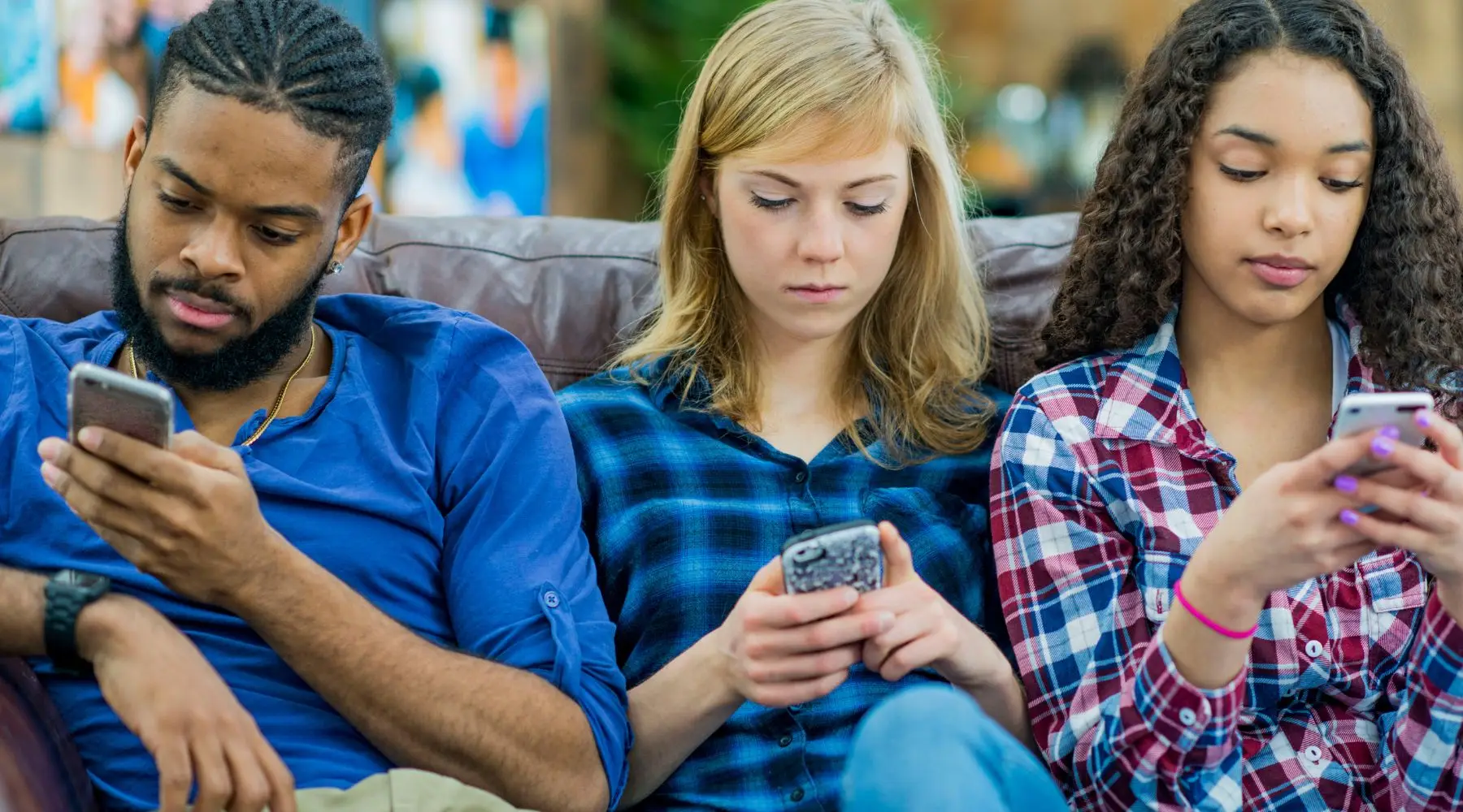 Three young adults are sitting on the couch and staring at their smartphones