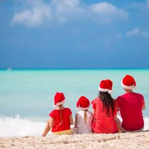 Family sitting on beach looking at sea wearing Santa's hats