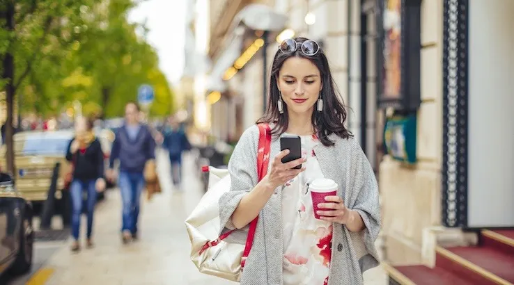 Smiling woman standing on a city street, looking at her phone. Image: Getty Images