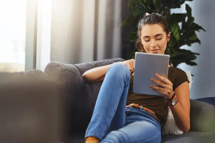 Shot of a young woman using her digital tablet while relaxing on a couch at home