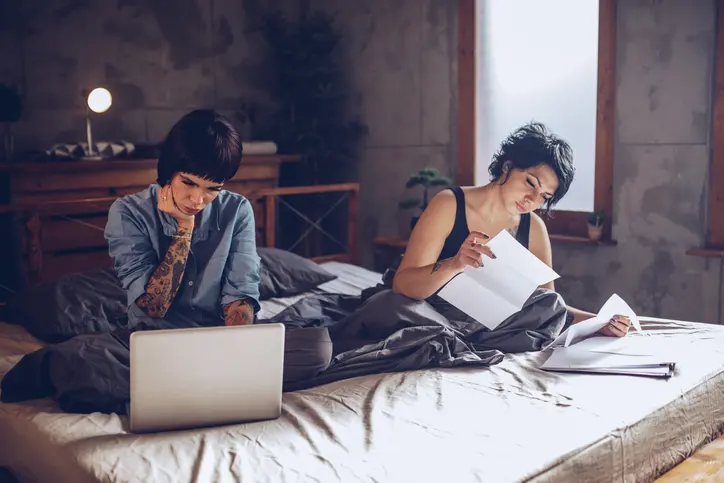 Young female couple calculating bills and tax expenses in bedroom