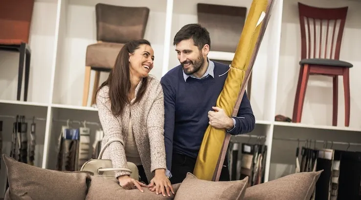 A woman and man smiling at each other and leaning on a lounge in a furniture store.