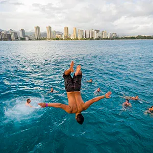 Group watching guy flip into water with Honolulu as backdrop