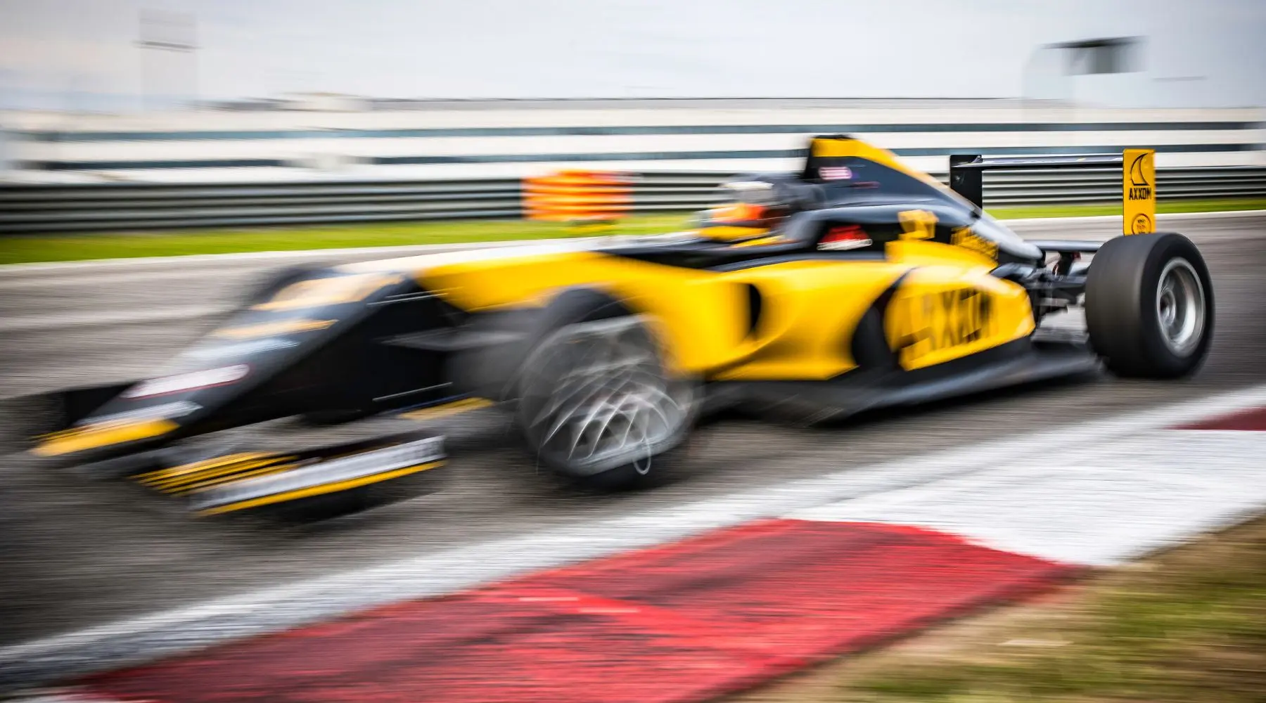 Blurred motion of a yellow open-wheel formula one race car go fast on a race track.