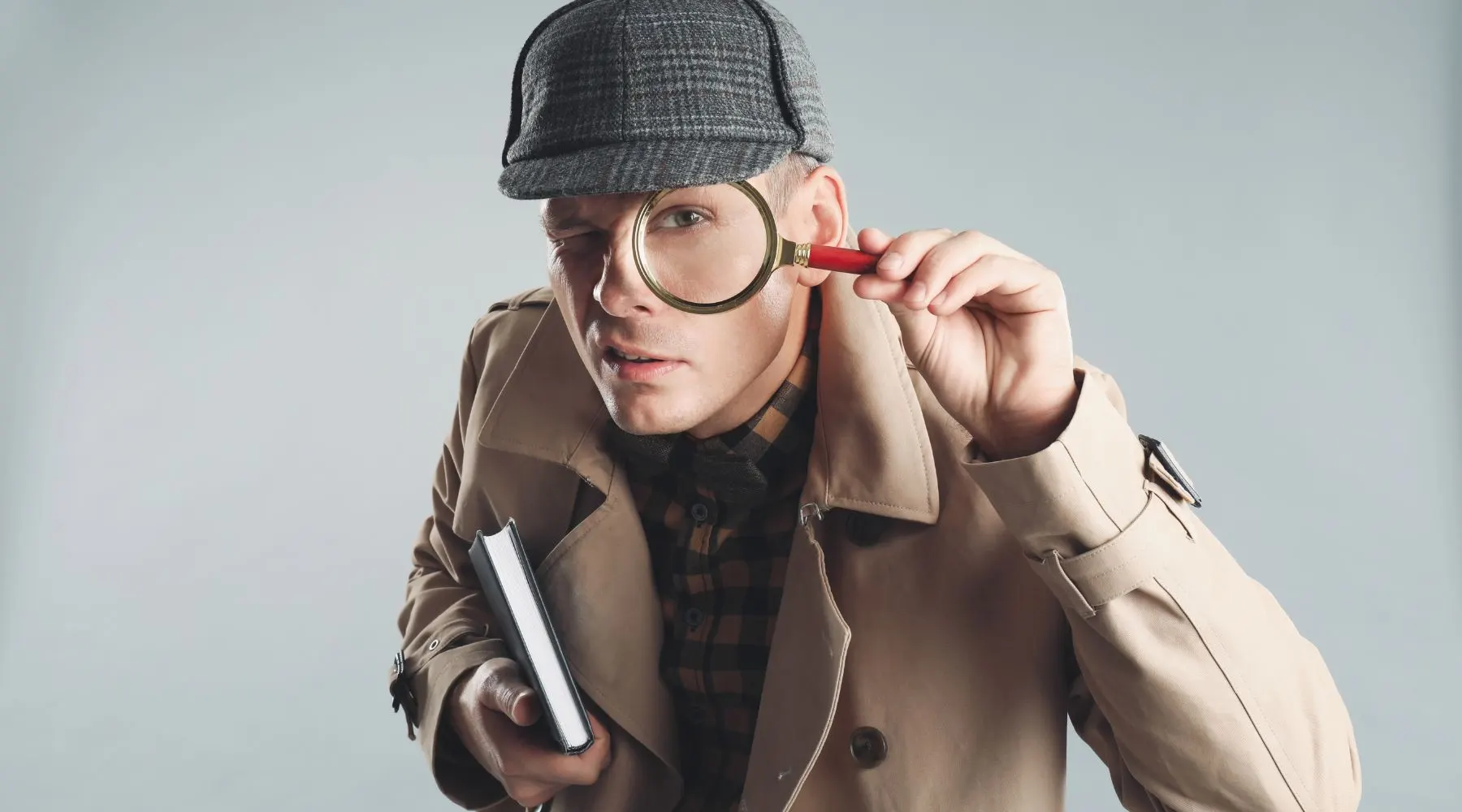 Male Detective Looking through Magnifying Glass on Grey Background