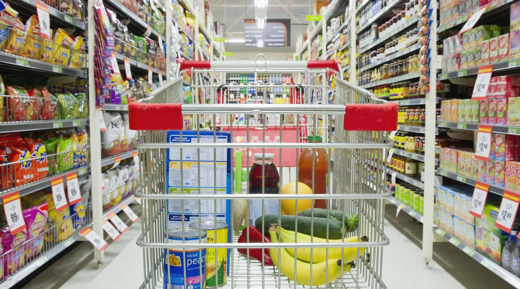 Grocery trolley full of items in a grocery store isle. 
