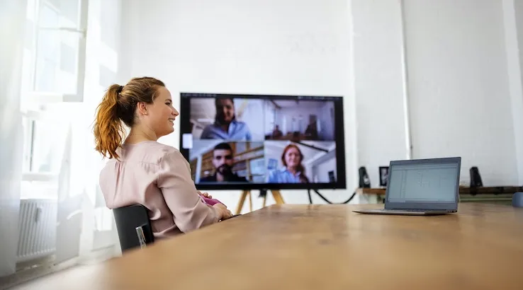An office meeting room with four staff attending via video.
