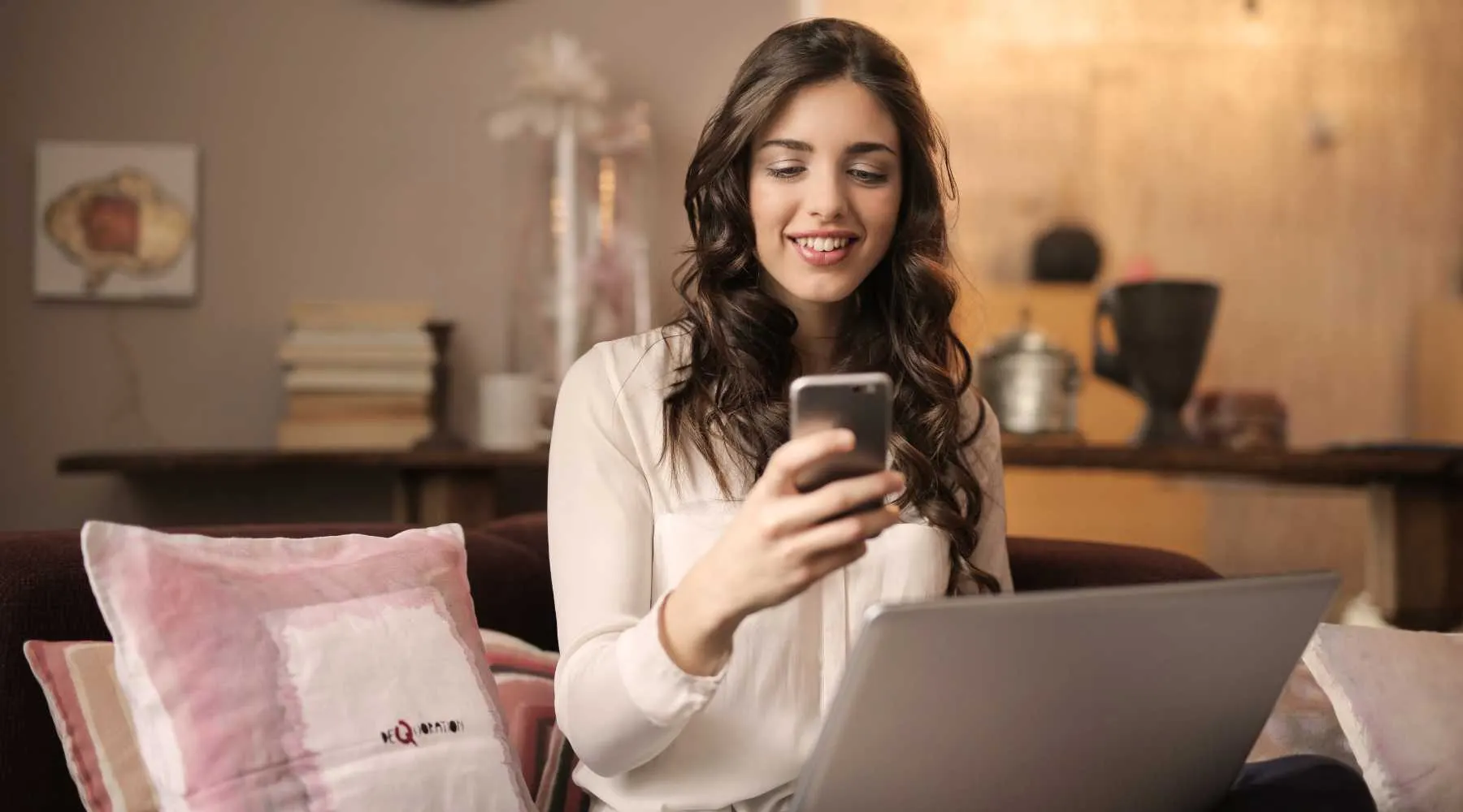 Woman holding a mobile phone and working on a laptop