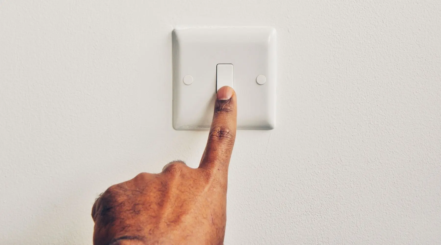 A man reaches to flick a light switch.