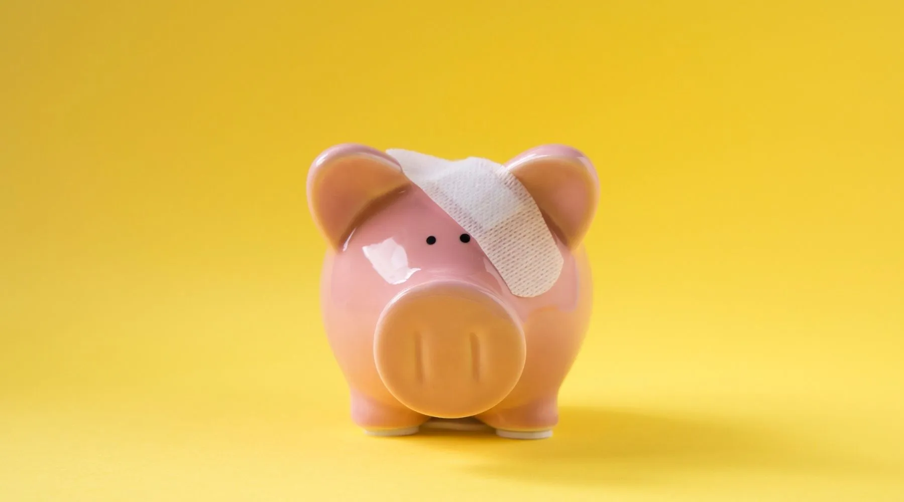 A piggy bank sits with a bandage over its head.