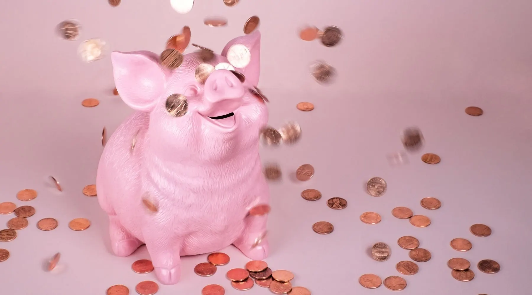 Piggy bank on a pink background, with coins falling around it.