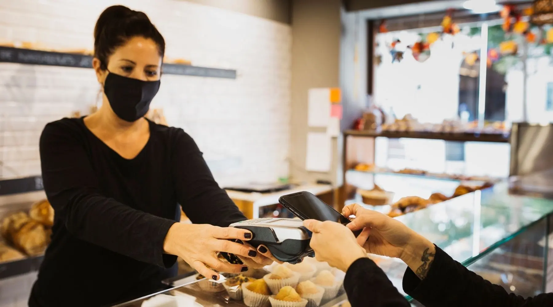 A person pays using their phone, the cashier wears a mask.