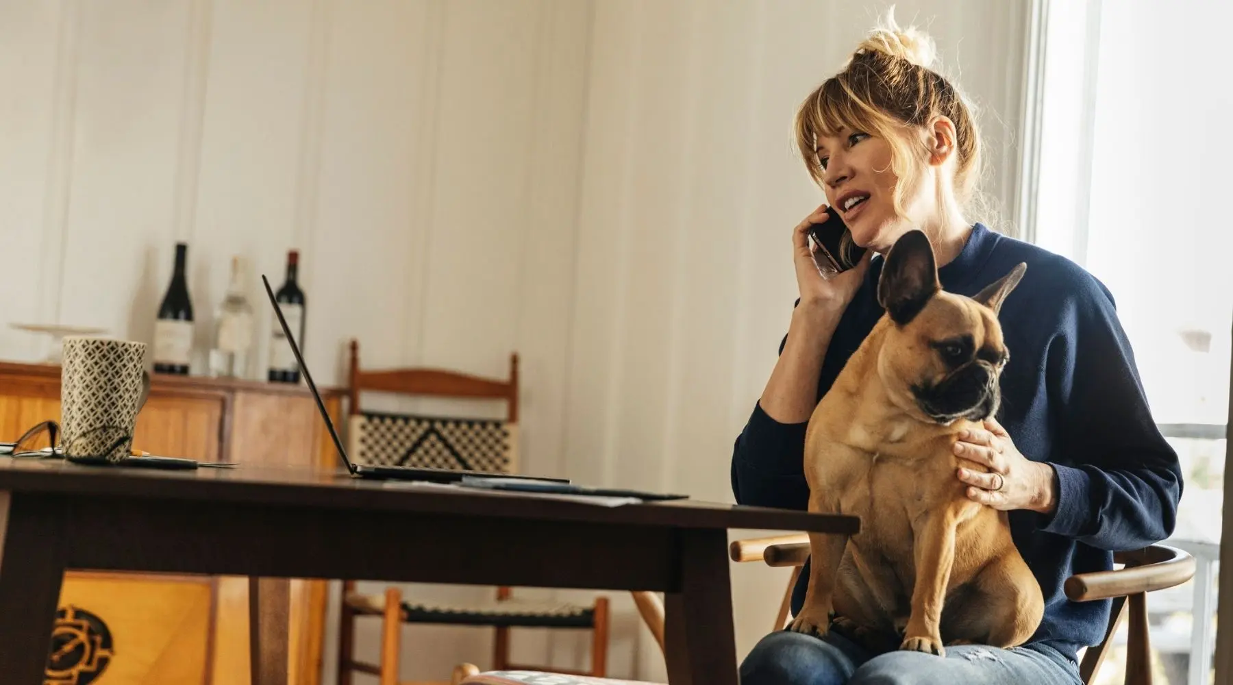 A woman talks on the phone with her dog sitting on her lap.