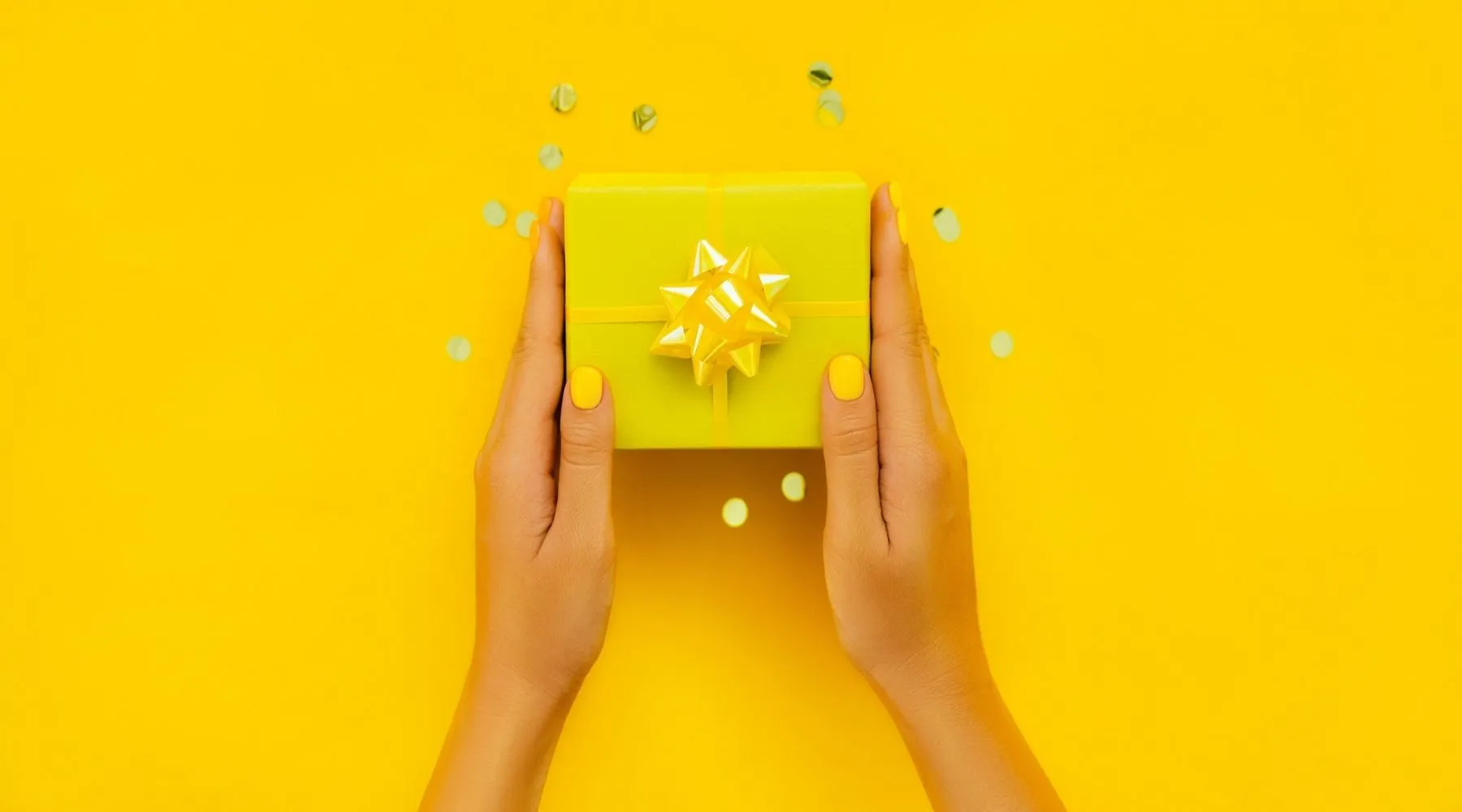 A pair of hands hold a yellow gift box, on a yellow background.