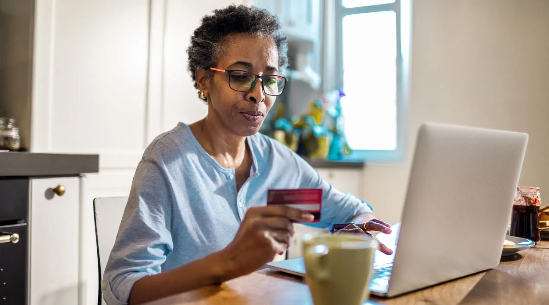 A mature woman sits at her laptop holding a credit card.