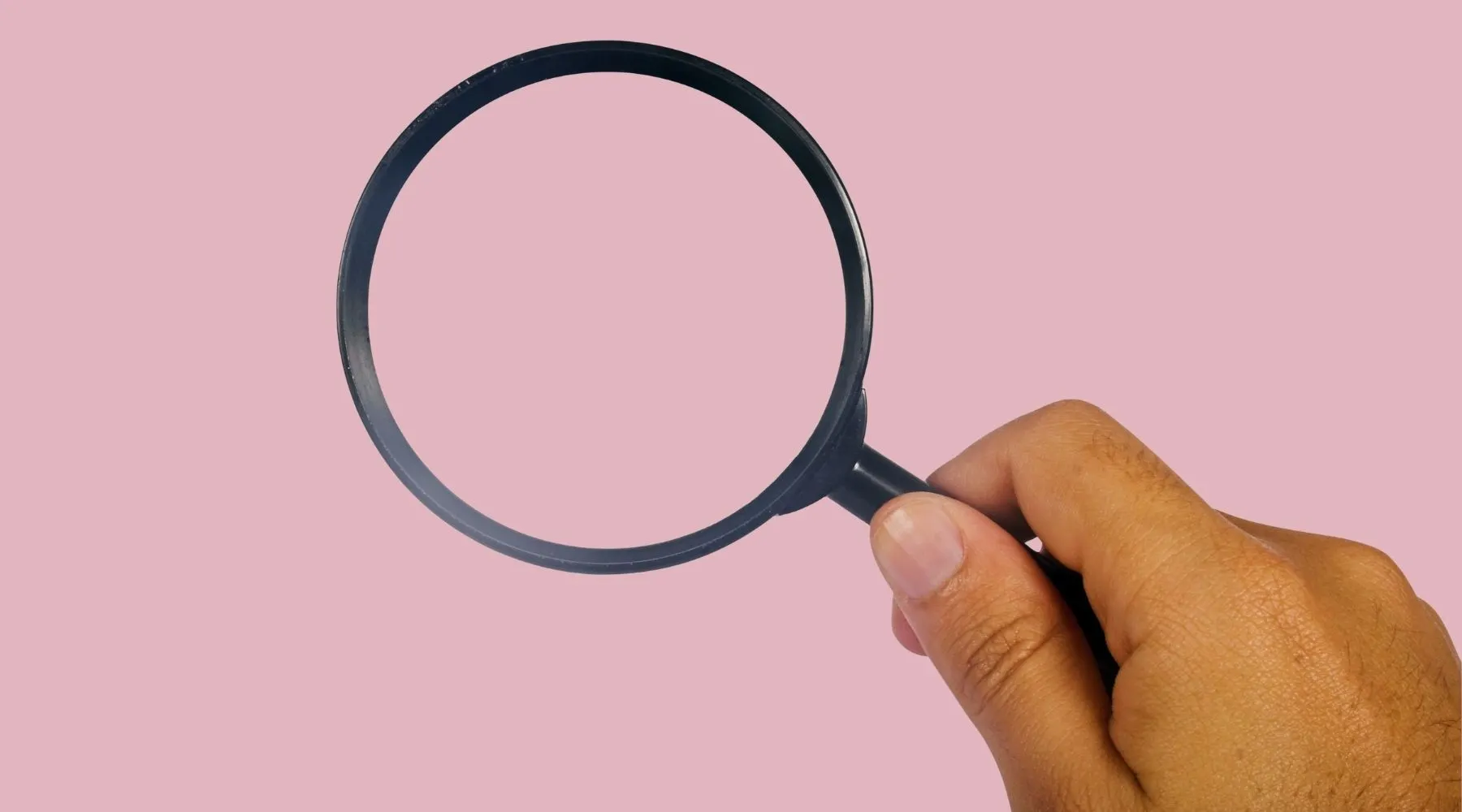 A man's hand holding a magnifying glass on a pink background.