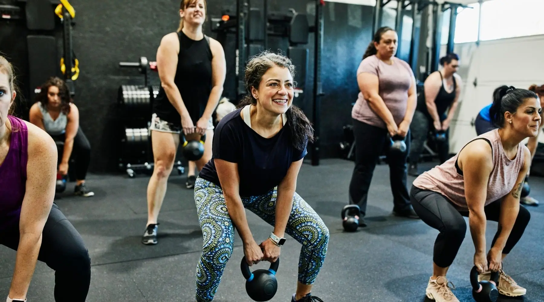 Smiling woman doing kettlebell swings while working out during class in gym.