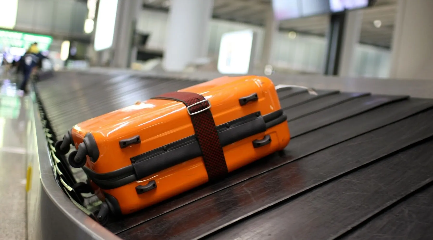 A lone orange suitcase on a luggage carousel