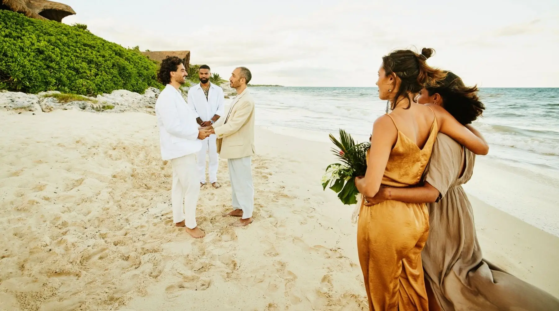 Wide shot of smiling gay couple getting married in front of friends and family at tropical beach resort
