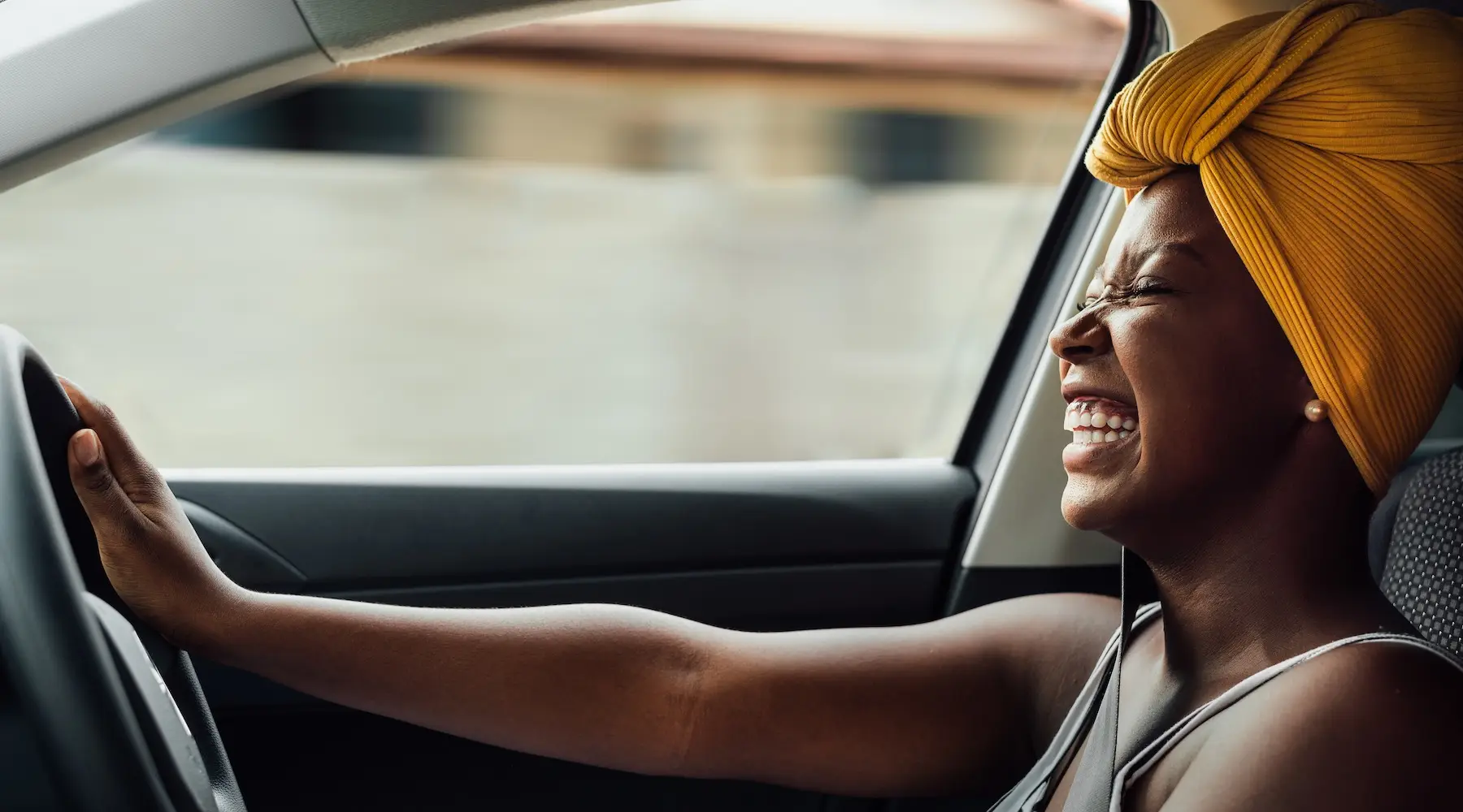 A woman with brown skin smiling as she drives a car