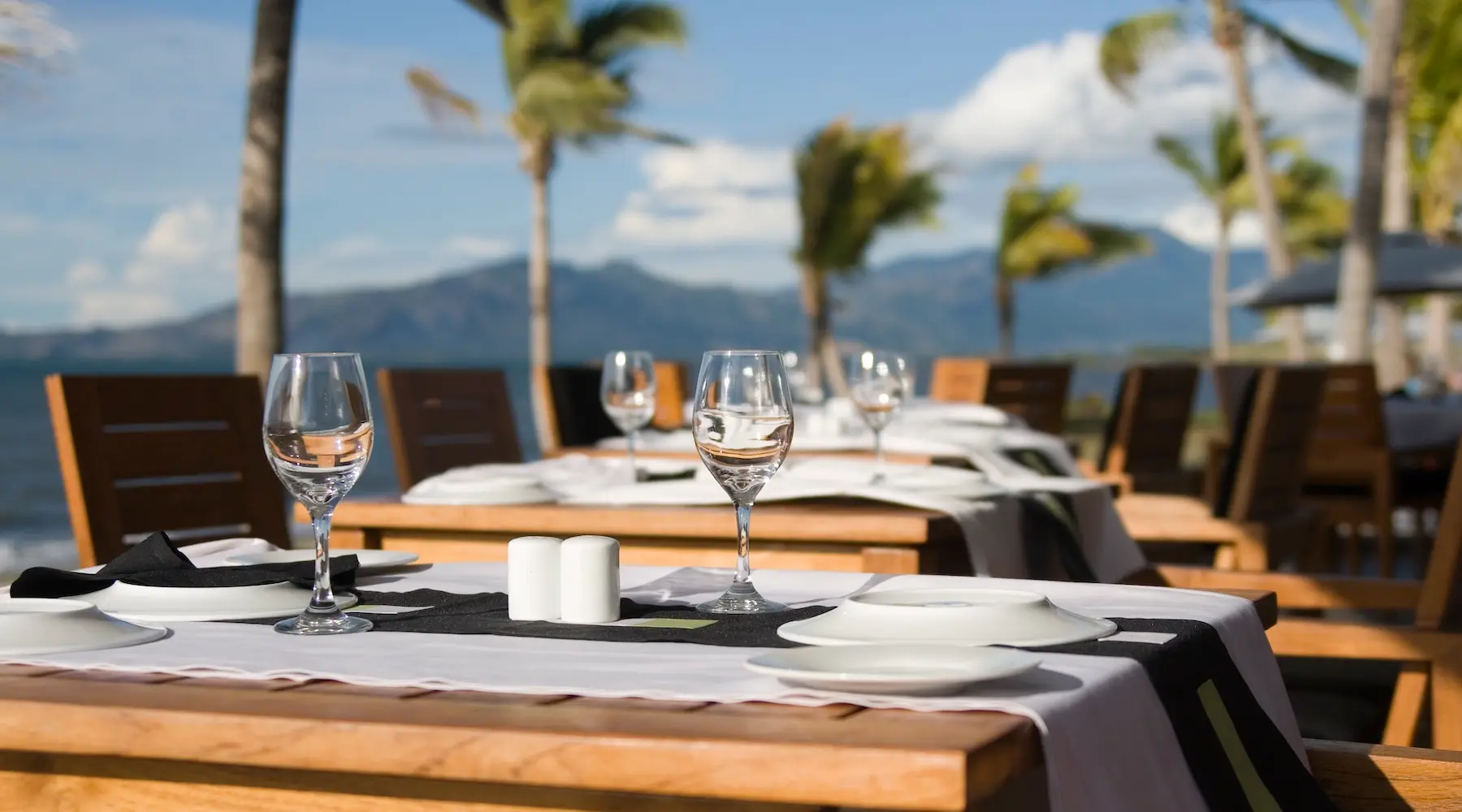A tropical dinner setting at a restaurant in a Fiji Resort, with palm trees and mountains in the distance.