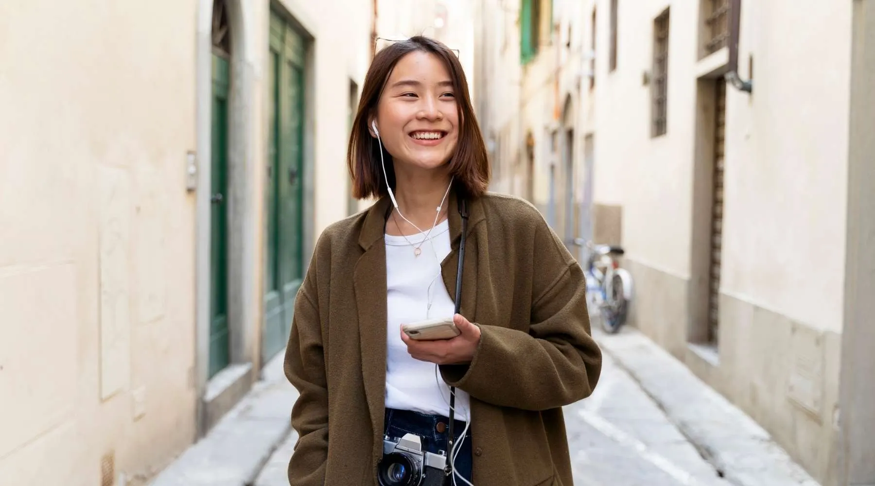 Italy, Florence, happy young woman with earphones and cell phone in an alley