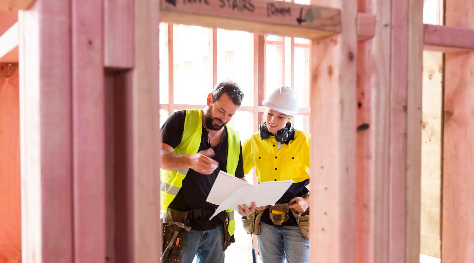 Two people in high-vis clothes looking at building plans on a construction site.