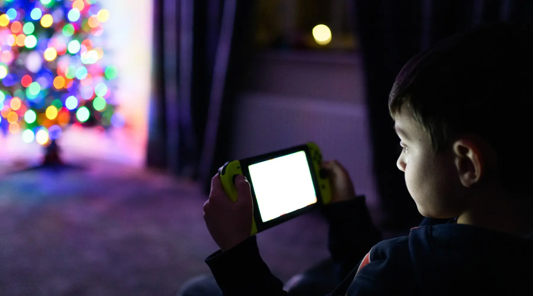 A child gaming by the light of the Christmas tree