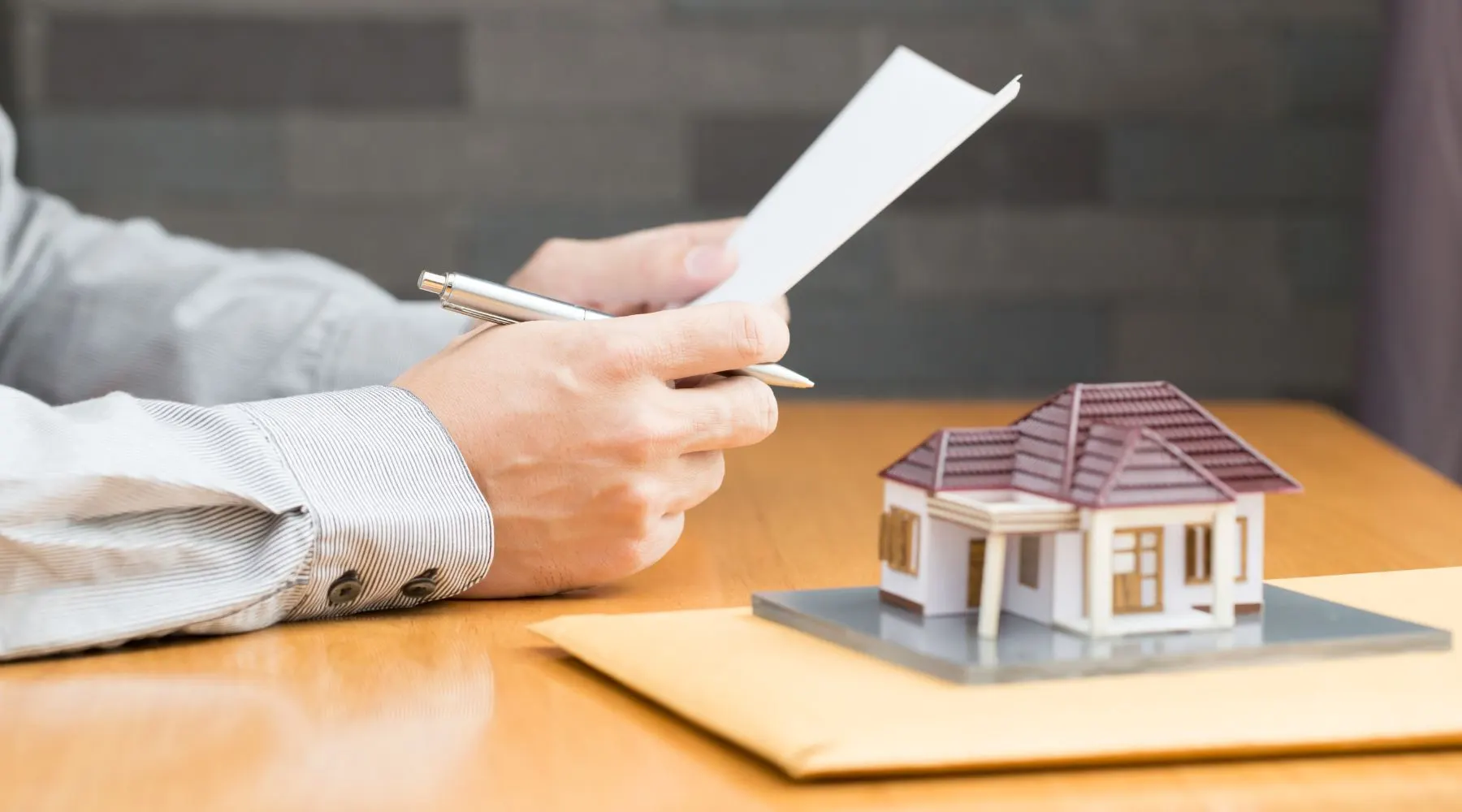 person holding a piece of paper with a tiny house model on the desk