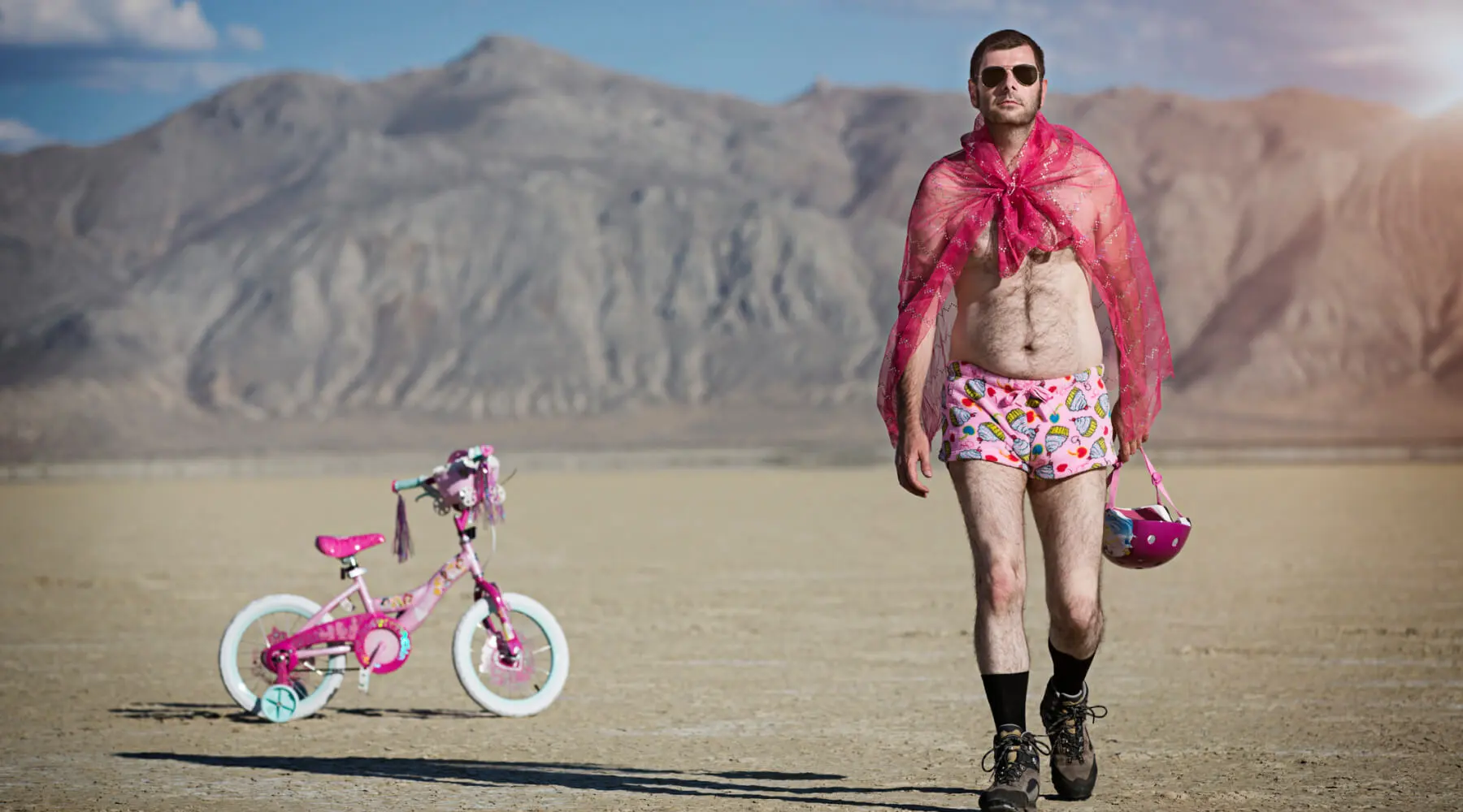 Man in pink shorts and towel strolling beside a pink bike.