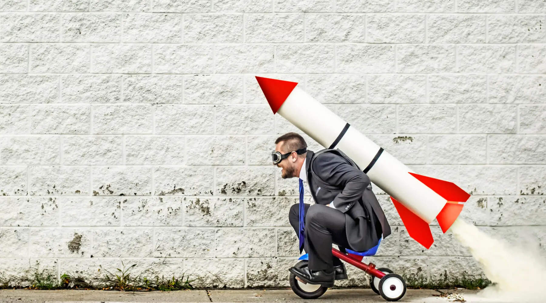 Man in suit riding a mini tricycle with a rocket on his back