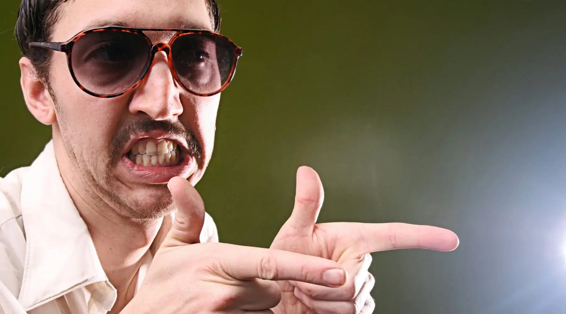 A man wearing sunglasses pointing directly at the camera